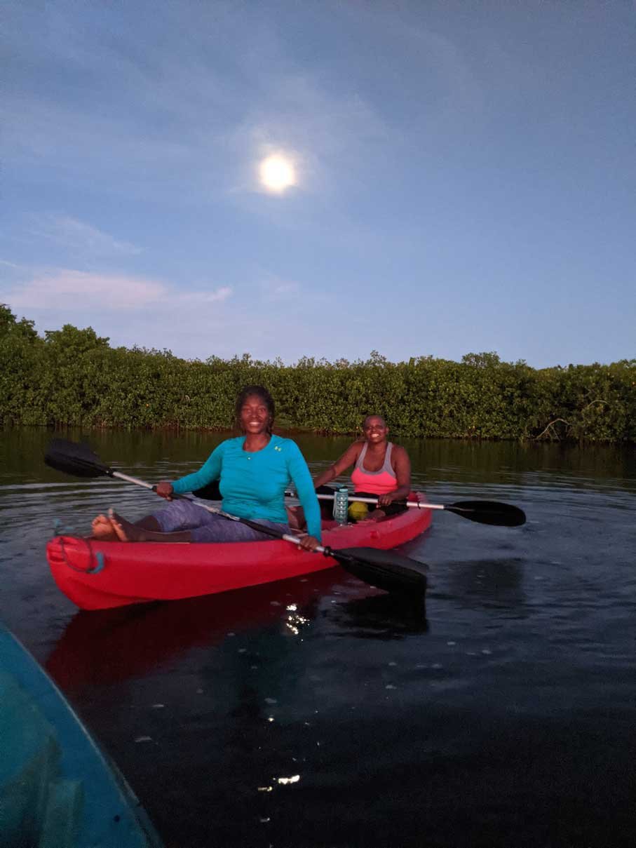 Two kayakers under a full moon on the lagoon at night, Hopkins, Belize