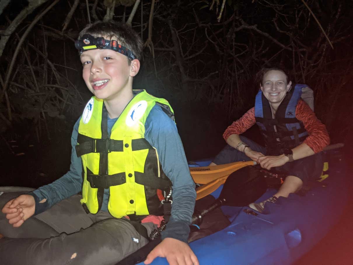 Young guest in a life vest kayaking the lagoon at night, Hopkins, Belize