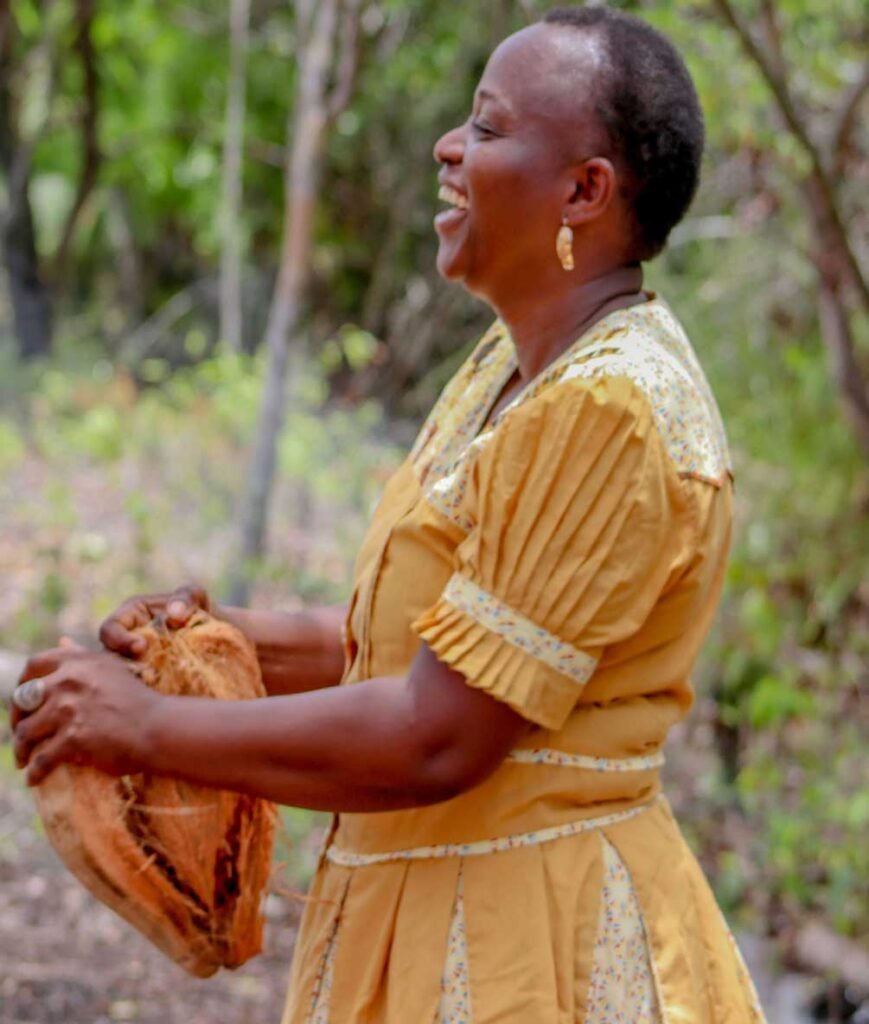 Uwahnie Martinez laughing in a gold Garifuna dress while holding a coconut