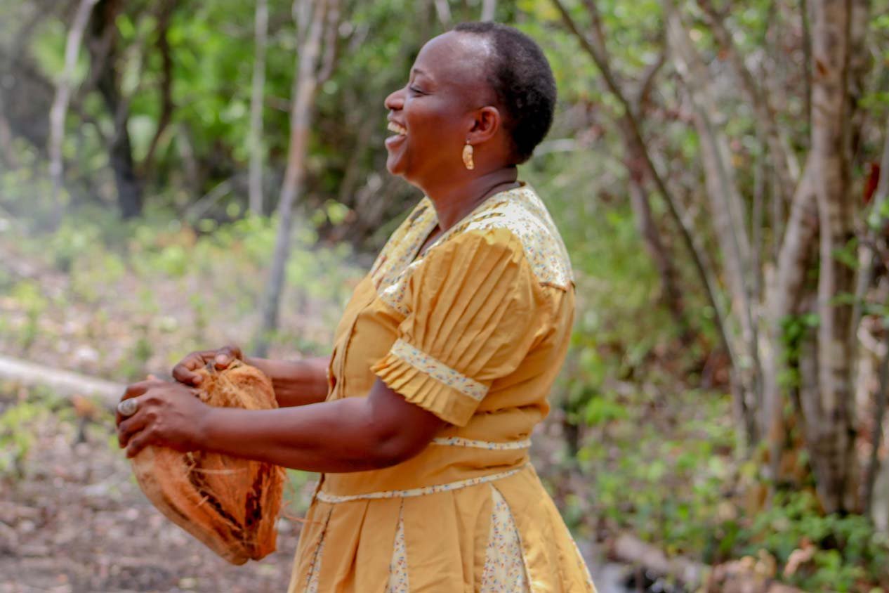Uwahnie Martinez, who founded Palmento Grove, laughing in a gold Garifuna dress while holding a coconut