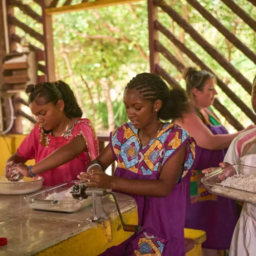 Guests in traditional dress preparing food together at Palmento Grove, Hopkins, Belize