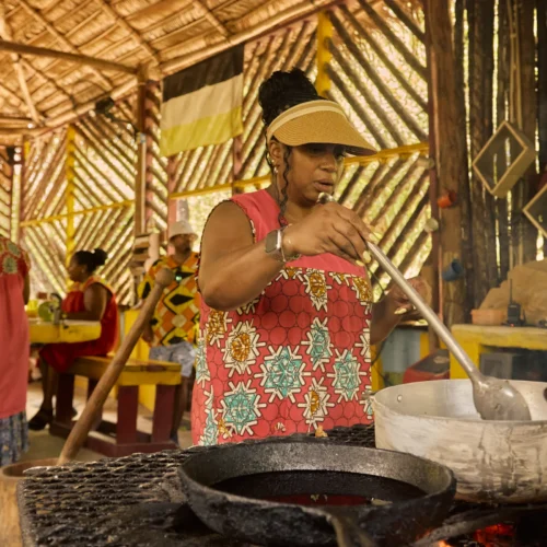 Two people working a wooden mortar and pestle in the yard at Palmento Grove, Hopkins, Belize