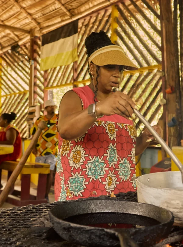 Two people working a wooden mortar and pestle in the yard at Palmento Grove, Hopkins, Belize