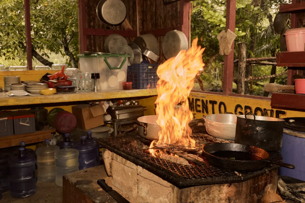 Tall flames under a cast-iron pan on the open-fire hearth at Palmento Grove, Hopkins, Belize