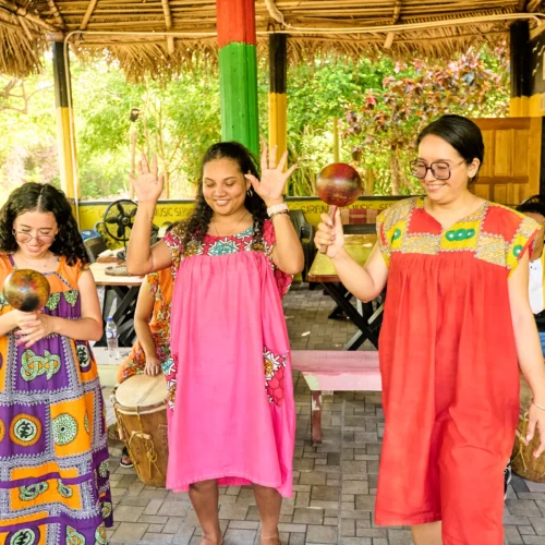 Guests dancing with raised hands and maracas in the drum pavilion at Palmento Grove, Hopkins, Belize