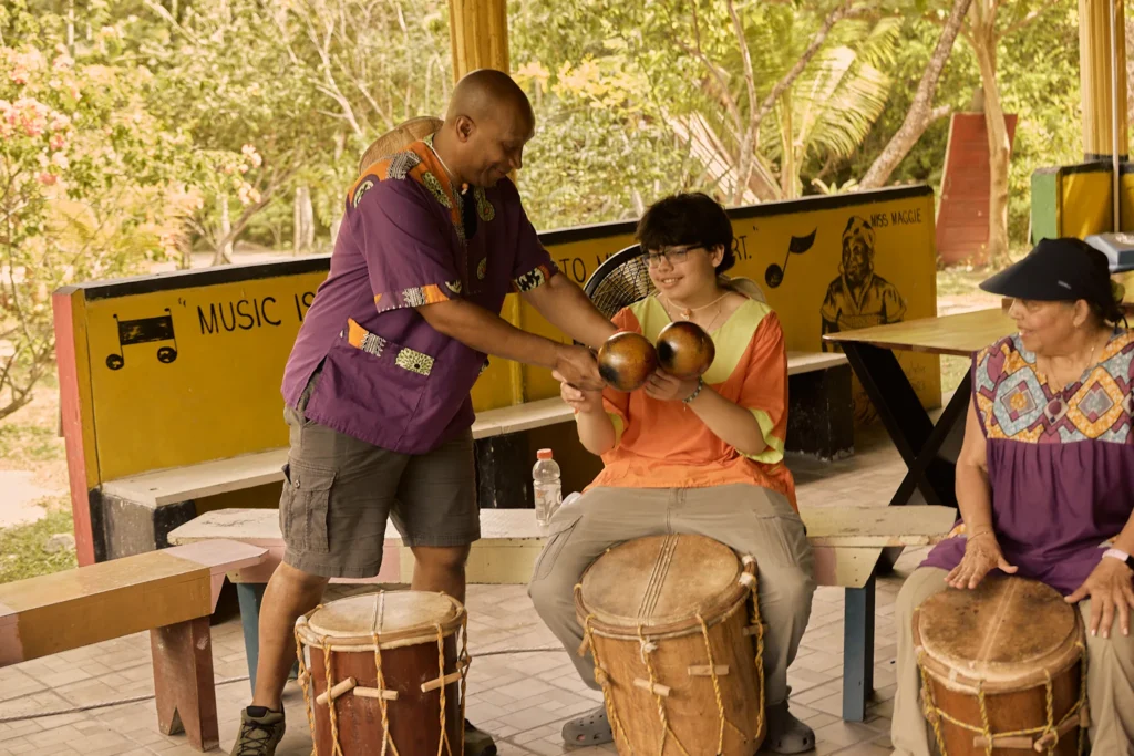 An instructor guiding a guest's hands on the primero drum at Palmento Grove, Hopkins, Belize