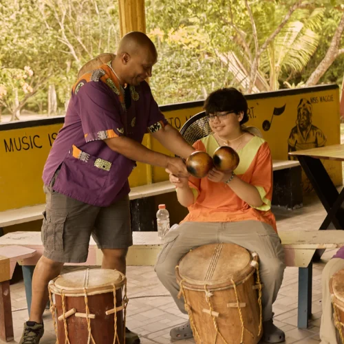 An instructor guiding a guest's hands on the primero drum at Palmento Grove, Hopkins, Belize