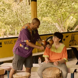 A Garifuna drumming instructor guiding a guest's hands on the drum at Palmento Grove, Hopkins, Belize