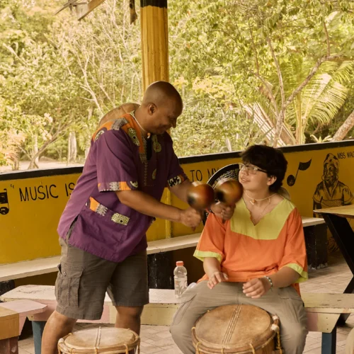 A Garifuna drumming instructor guiding a guest's hands on the drum at Palmento Grove, Hopkins, Belize