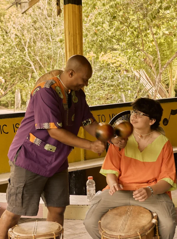 A Garifuna drumming instructor guiding a guest's hands on the drum at Palmento Grove, Hopkins, Belize