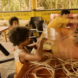 Hands weaving a basket from reeds during a craft session at Palmento Grove, Hopkins, Belize