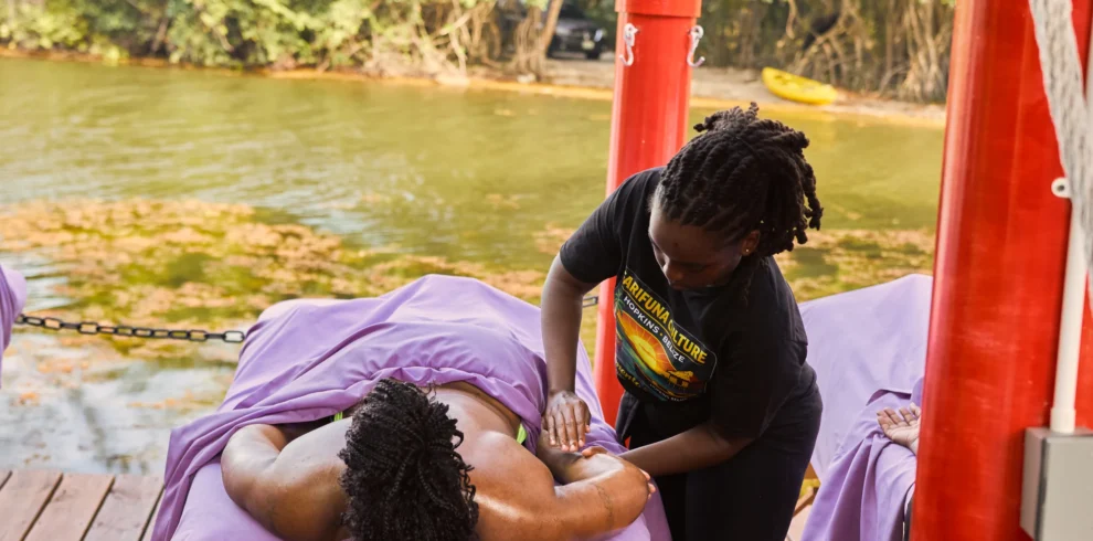 A Palmento Grove therapist working on a guest's shoulders on the massage deck over Fresh Water Creek Lagoon, Hopkins, Belize